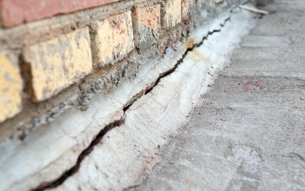 Deep crack in concrete foundation at the base of a brick wall from water and settlement